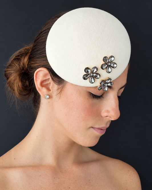 Model wearing the Mini Émillie percher hat adorned with three silver-toned flower brooches embellished with dark rhinestones.