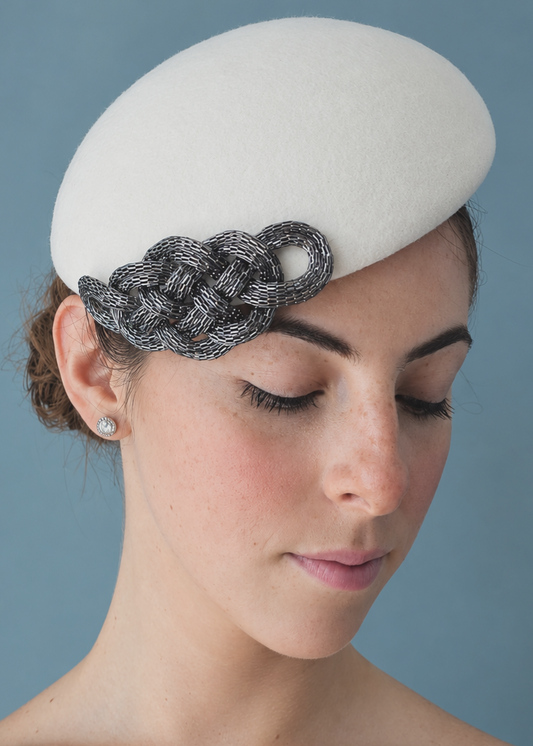 Zoé Percher structured white felt hat with a silver textured braided accent on the side, set against a solid blue-gray background.