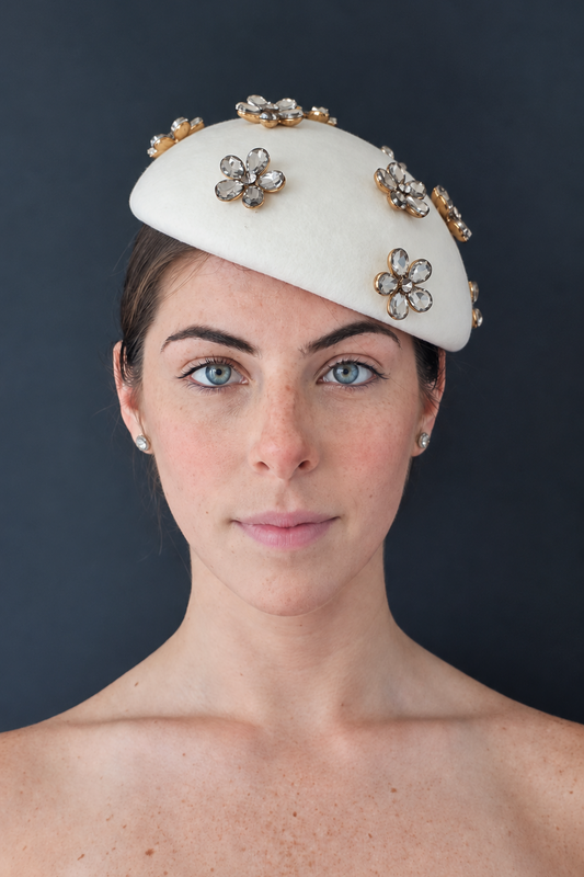 Model wearing the Émillie percher hat adorned with gold and crystal flower embellishments, set against a dark gray background.