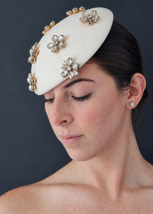 Side portrait of model wearing the Émillie percher hat adorned with gold and crystal flower embellishments, set against a dark gray background.