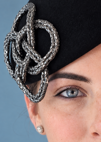 Close-up Fleur Percher fascinator hat with a large silver braided knot embellishment.