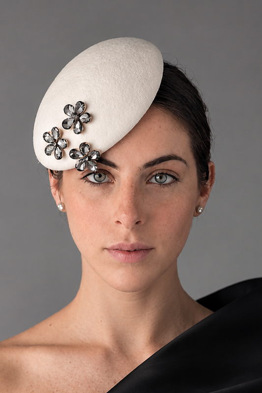 Model wearing the Mini Émillie percher hat adorned with three silver-toned flower brooches embellished with dark rhinestones. 