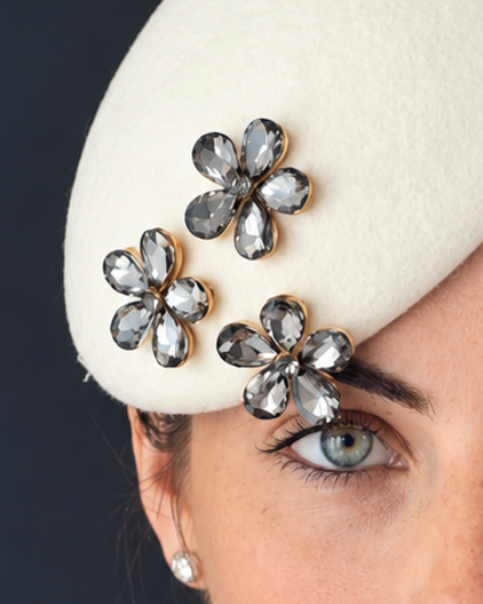 Close up of model wearing the Mini Émillie percher hat adorned with three silver-toned flower brooches embellished with dark rhinestones. 