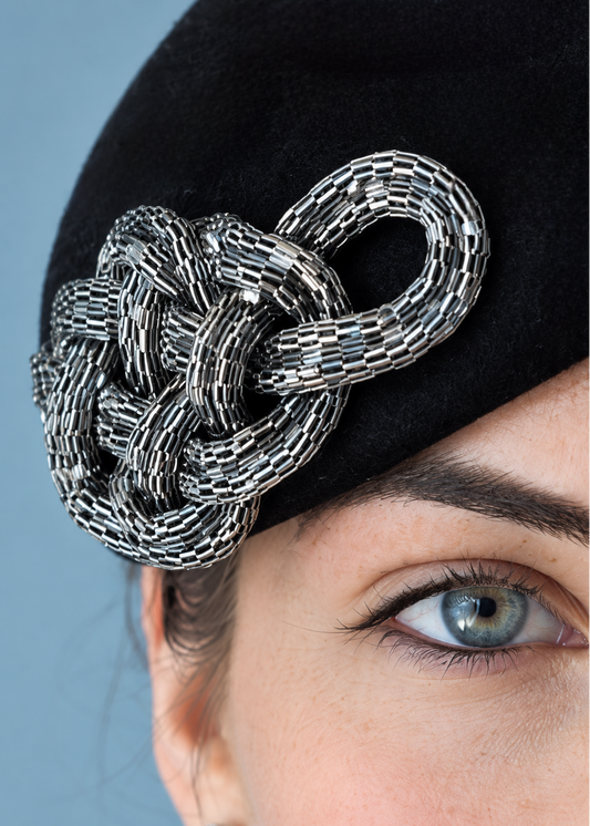 Close up of the Zoé wool felt percher hat with a silver chain-link decorative accent, photographed against a solid light blue background.